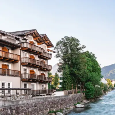 Das HENRI Hotel Kitzbühel von außen neben einem Fluss und Bäumen.